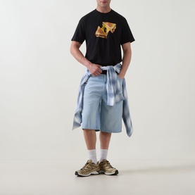Model wearing Carhartt Cheese Toast T-Shirt in black with graphic print, styled with light blue shorts and a tied shirt at the waist.
