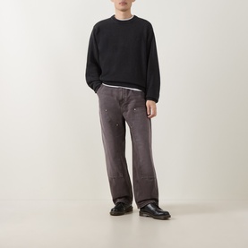 Model wearing Carhartt Kori Logo Knit Sweater in black with crew neck, styled with dark grey wide-leg jeans and black leather shoes.