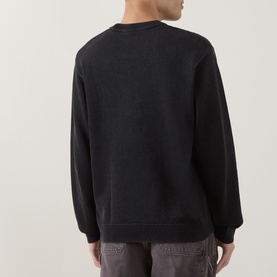 Model wearing Carhartt Kori Logo Knit Sweater in Black, crew neck, long sleeves, ribbed trims, back view, styled with grey trousers.