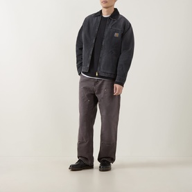Model wearing Carhartt Kori Logo Knit Sweater in Black, styled with dark zip jacket, grey trousers and black boots.
