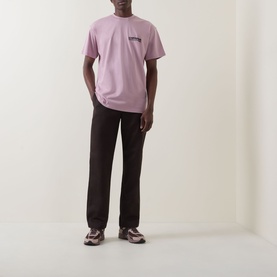 Model wearing Carhartt Cubist Logo T-Shirt in Hortensia pink with dark brown trousers and chunky trainers.