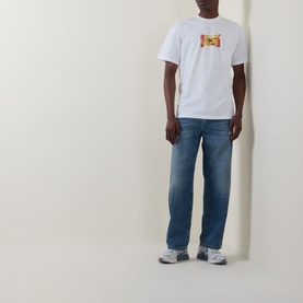 Model wearing Carhartt Road Side Snack T-Shirt in white with chest graphic, styled with mid-wash jeans and grey trainers.