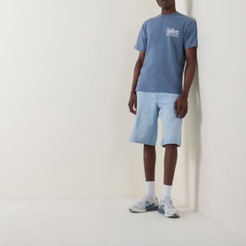 Model wearing Carhartt Formidable Logo T-Shirt in Shady Blue with light wash denim shorts and grey trainers.