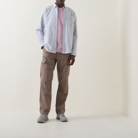 Model wearing Carhartt Pocket Logo T-Shirt in Hortensia pink, styled with a light blue overshirt, brown cargo trousers and grey trainers.