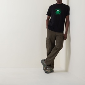 Model wearing Carhartt Please Don't Snitch Logo T-Shirt in black with green graphic, styled with olive cargo trousers and chunky trainers.