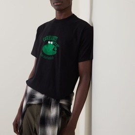 Model wearing Carhartt Please Don't Snitch Logo T-Shirt in black with green frog graphic, styled with a plaid shirt tied at the waist.