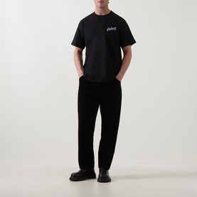 Model wearing Carhartt Pup Logo T-Shirt in black with small chest logo, paired with black trousers and black chunky sole shoes.