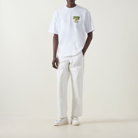 Model wearing Carhartt Pinball Logo T-Shirt in white with crew neck and chest graphic, styled with cream trousers and white trainers.