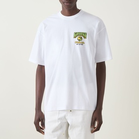 Model wearing Carhartt Pinball Logo T-Shirt in white with small chest graphic, crew neck, short sleeves, styled with cream trousers