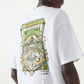 Model wearing Carhartt Pinball Logo T-Shirt in white, showing back graphic of pinball machine illustration in green and yellow tones.