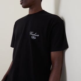 Model wearing Carhartt Gracious Logo T-Shirt in black with white script chest embroidery, crew neck, short sleeves, and dropped shoulders.
