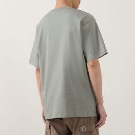 Model wearing Carhartt Madison Logo T-Shirt in Shady Green, rear view, short sleeves, straight hem, styled with brown trousers.