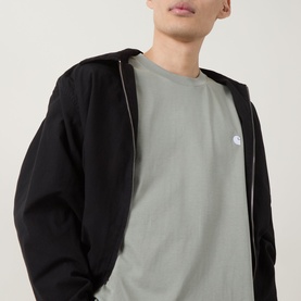 Model wearing Carhartt Madison Logo T-Shirt in Shady Green with white embroidered chest logo, styled with a black zip-up jacket.