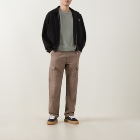 Model wearing Carhartt Madison Logo T-Shirt in Shady Green/White, styled with black zip jacket, taupe cargo trousers and navy trainers.