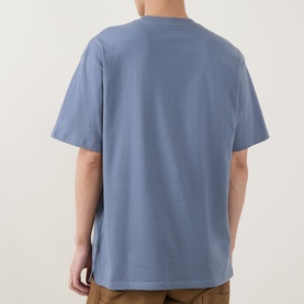 Model wearing Carhartt Crew Neck T in Shady Blue, rear view, relaxed fit, short sleeves, styled with tan trousers.
