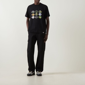 Model wearing Carhartt Coordinates Logo T-Shirt in black with graphic print, styled with black cargo trousers and grey trainers.