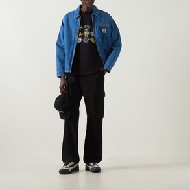 Model wearing Carhartt Coordinates Logo T-Shirt in Black with blue denim jacket, black cargo trousers, and grey trainers.