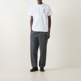 Model wearing Carhartt Playing Cards Logo T-Shirt in white with small chest graphic, styled with grey trousers and black shoes.