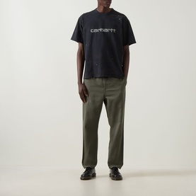 Model wearing Carhartt Painter Logo T-Shirt in black with script logo, styled with olive green trousers and black loafers.