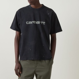 Model wearing Carhartt Painter Logo T-Shirt in black with distressed finish and script logo, styled with khaki trousers.