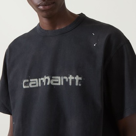 Model wearing Carhartt Painter Logo T-Shirt in black with distressed script logo print and paint splatter detail at chest.