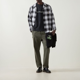 Model wearing Carhartt Painter Logo T-Shirt in Black under black and white plaid shirt, styled with olive trousers and black shoes.