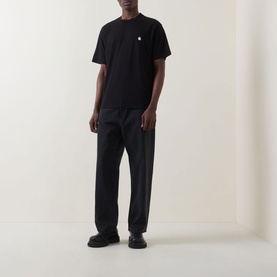 Model wearing Carhartt Madison Logo T-Shirt in black with white embroidered logo, styled with black straight-leg trousers and black chunky shoes.