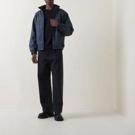 Model wearing Carhartt Madison Logo T-Shirt in Black/White, styled with a dark check bomber jacket and black wide-leg trousers.