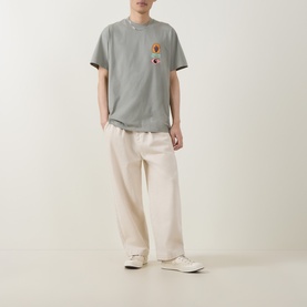 Model wearing Carhartt Stacked Grapes Logo T-Shirt in Shady Green with cream wide-leg trousers and white trainers.