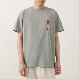 Model wearing Carhartt Stacked Grapes Logo T-Shirt in Shady Green with chest graphic, styled with cream trousers.