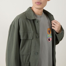Model wearing Carhartt Stacked Grapes Logo T-Shirt in Shady Green, styled with a matching olive shirt jacket featuring a graphic patch.