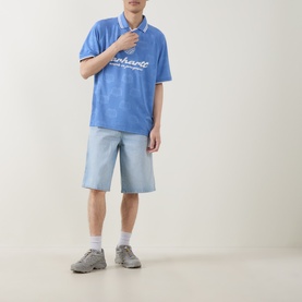 Model wearing Carhartt Terrace Logo Football T-Shirt in Curacao blue with polo collar and script logo, styled with light denim shorts and grey