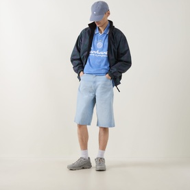 Model wearing Carhartt Terrace Logo Football T-Shirt in Curacao blue, styled with navy jacket, light denim shorts, white socks and grey trainers.