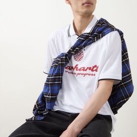 Model wearing Carhartt Heart Train/White crew neck T-shirt with embroidered logo, styled with a blue plaid shirt draped over shoulders.