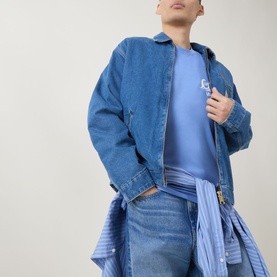 Model wearing Carhartt Waves Logo T-Shirt in Curacao blue, styled with a denim jacket and jeans, waves graphic visible on chest.