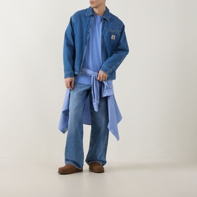 Model wearing Carhartt Waves Logo T-Shirt in Curacao blue, styled with denim jacket, wide-leg jeans, and striped shirt tied at waist.