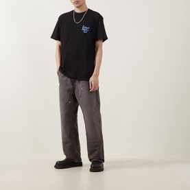 Model wearing Carhartt Waves Logo T-Shirt in black with small chest graphic, styled with dark grey wide-leg trousers and a chain necklace.