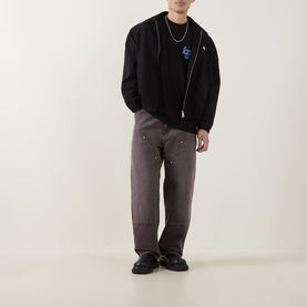 Model wearing Carhartt Waves Logo T-Shirt in Black, styled with grey paint-splatter trousers, gold chain necklace and black loafers.