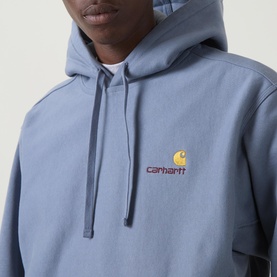 Model wearing Carhartt American Script Logo Hoodie in Shady Blue, showing embroidered chest logo and drawstring hood detail.