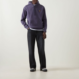 Model wearing Carhartt American Script Logo Hoodie in Shady Purple with black straight-leg jeans and grey trainers.