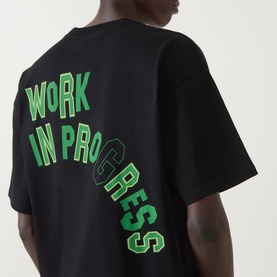 Model wearing Carhartt Built Different Logo T-Shirt in black, showing back with green Work In Progress graphic print.