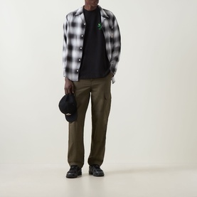 Model wearing Carhartt Built Different Logo T-Shirt in Black under grey check overshirt, with khaki cargo trousers and black boots.