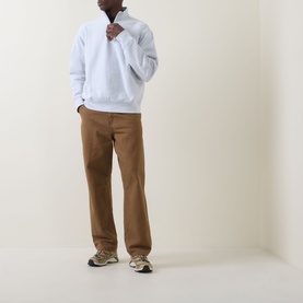 Model wearing Carhartt American Script Logo Half-Zip Sweatshirt in Ash Heather, styled with tan trousers and grey trainers.