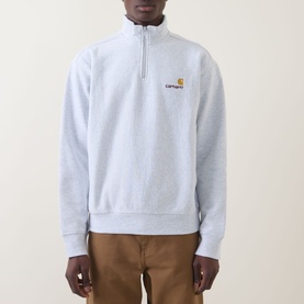 Model wearing Carhartt American Script Logo Half-Zip Sweatshirt in Ash Heather, with gold embroidered chest logo, styled with tan trousers.