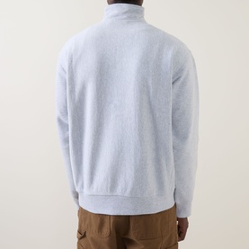 Model wearing Carhartt American Script Half-Zip Sweatshirt in Ash Heather, back view, ribbed hem and cuffs visible, styled with tan trousers.