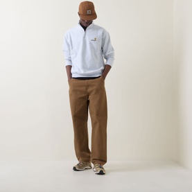 Model wearing Carhartt American Script Logo Half-Zip Sweatshirt in Ash Heather, styled with tan trousers, brown cap and chunky trainers.