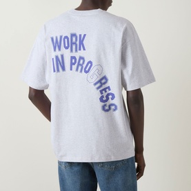 Model wearing Carhartt Built Different Logo T-Shirt in Ash Heather, showing back with blue Work In Progress graphic, paired with blue jeans