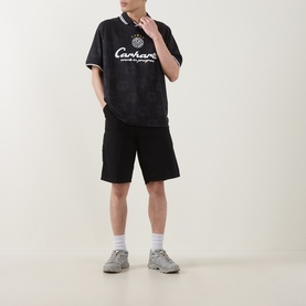 Model wearing Carhartt Heart Train Crew Neck T-Shirt in black with white logo, styled with black shorts and grey trainers.