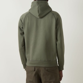 Model wearing Carhartt Chase Logo Hoodie in Leaf/Gold, rear view, showing adjustable hood, raglan sleeves and straight hem, styled with khaki