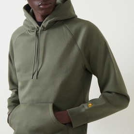 Model wearing Carhartt Chase Logo Hoodie in Leaf/Gold, close-up showing gold embroidered cuff logo, kangaroo pocket and drawstring hood.